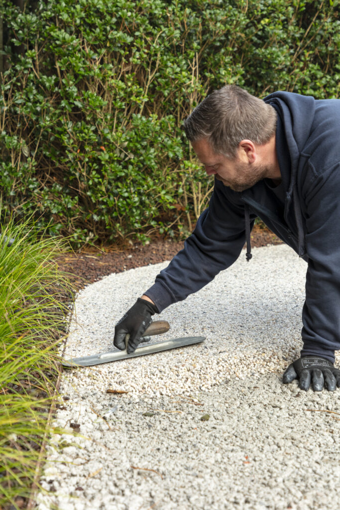 Een vakman van Floors & More smeert de waterdoorlatende Terradec met precisie op een oprit in Knokke.