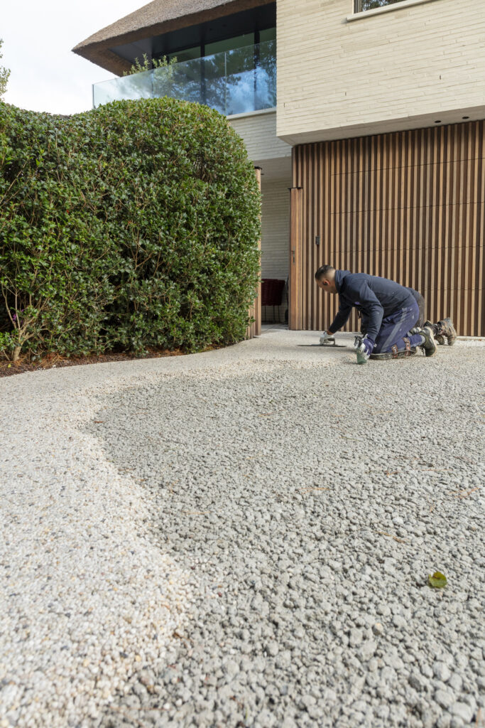 Onze arbeiders brengen de waterdoorlatende Terradec aan op de oprit, met op de achtergrond een moderne high-end woning.