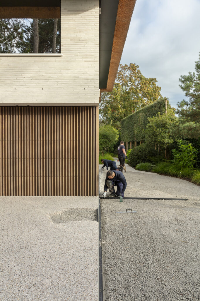 Vakmannen van Floors & More smeren de Terradec op de oprit, met een stijlvolle, moderne woning op de achtergrond.